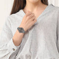 Lacoste horloge dames - LC2001220 met grijze wijzerplaat en metalen band, gedragen door vrouw in gestreepte blouse. Elegant dameshorloge van 38mm.